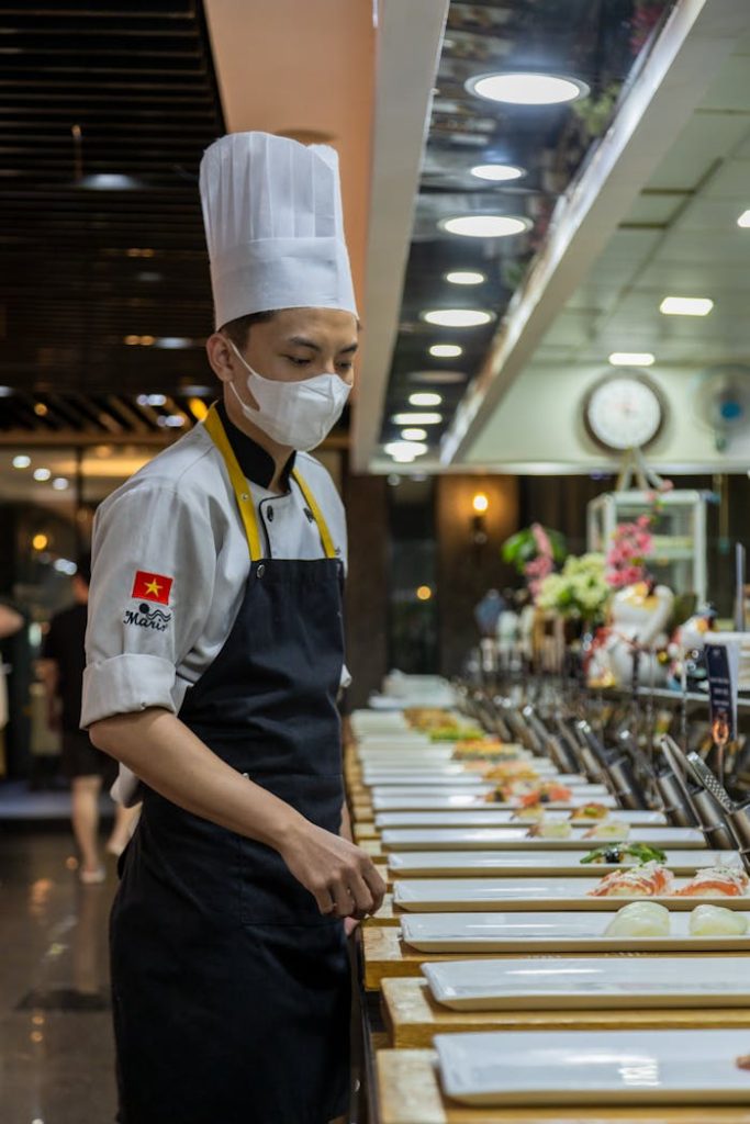 Chef in uniform preparing food in a busy restaurant kitchen with a focus on presentation.